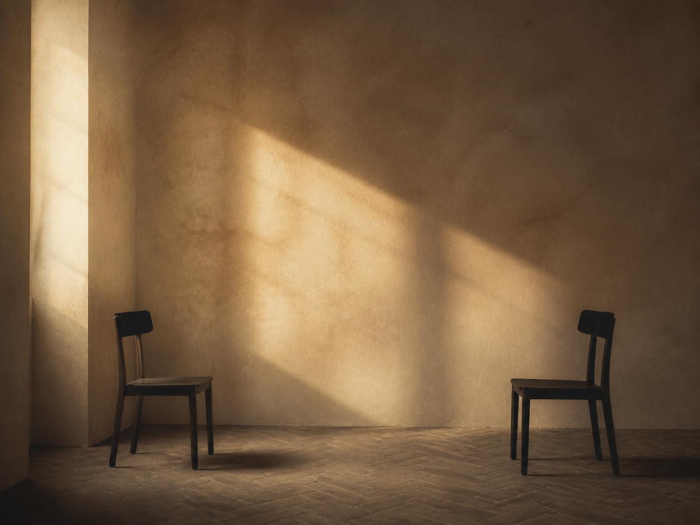 Habitación vacía con dos sillas de madera enfrentadas y luz lateral